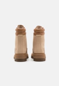 Botas de tobillo de ante color beige con un puño de cuero acolchado en el mismo tono. Las suelas tienen un patrón de goma marrón texturizado para mayor agarre y durabilidad.
