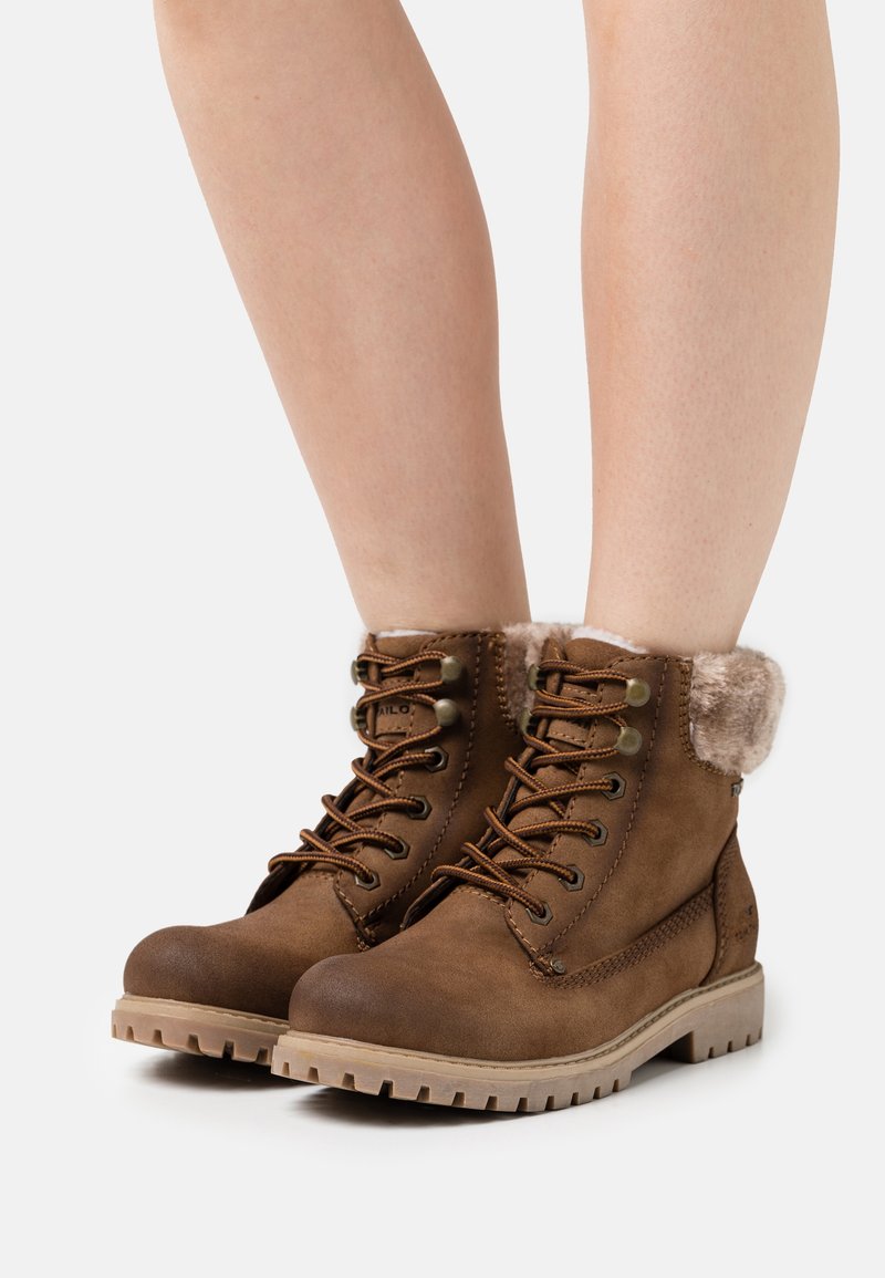 Bottes à lacets marron jusqu'à la cheville, avec doublure en fausse fourrure et suède texturé, équipées d'œillets en métal et d'une semelle en caoutchouc robuste.