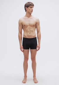 Μαύρα μαγιό σορτς από ελαστικό ύφασμα, με σχέδιο χαμηλής μέσης και μικρή πλαϊνή τσέπη. Λεία υφή και εφαρμοστό σχήμα.