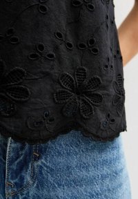 Top negro bordado con patrones florales, dobladillo en forma de ondas y superficie texturada, combinado con jeans de mezclilla azul claro.