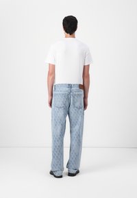 Jean en denim bleu clair avec un motif intégral, coupe décontractée et un patch en cuir sur la ceinture arrière. Porté avec un t-shirt blanc uni.