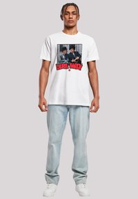 White cotton t-shirt featuring a graphic print of two men in hats, with red text "Laurel & Hardy" beneath the image. Worn with light jeans and sneakers.