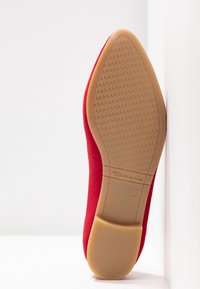 Chaussure à talons hauts en daim rouge avec un dessus lisse et une semelle en caoutchouc beige texturée, comportant un logo de la marque et une taille embossés au fond.