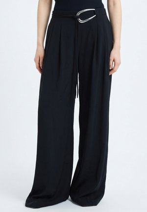 Persona che indossa pantaloni neri larghi e larghi con cintura in tessuto con fibbia argentata, abbinati a un top nero.