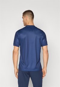 T-shirt de sport bleu marine à manches courtes, en tissu lisse, col rond et texture subtile sur les épaules. Vue arrière montrée.