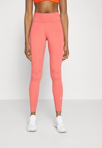 Leggings sportivi rosa con vita alta e una texture di tessuto liscia. Presenta un piccolo logo Nike bianco sulla parte bassa della gamba sinistra.