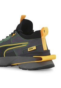 Schwarzer und grüner Puma Sneaker mit gelben Akzenten, texturiertem Sohlendesign und Zuglasche am Fersenbereich, von hinten und seitlich auf einem weißen Hintergrund dargestellt.