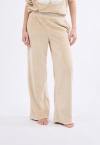 Pantalons de détente en polaire beige avec une coupe évasée, une texture douce et une taille élastique, sans motifs ni éléments métalliques visibles.