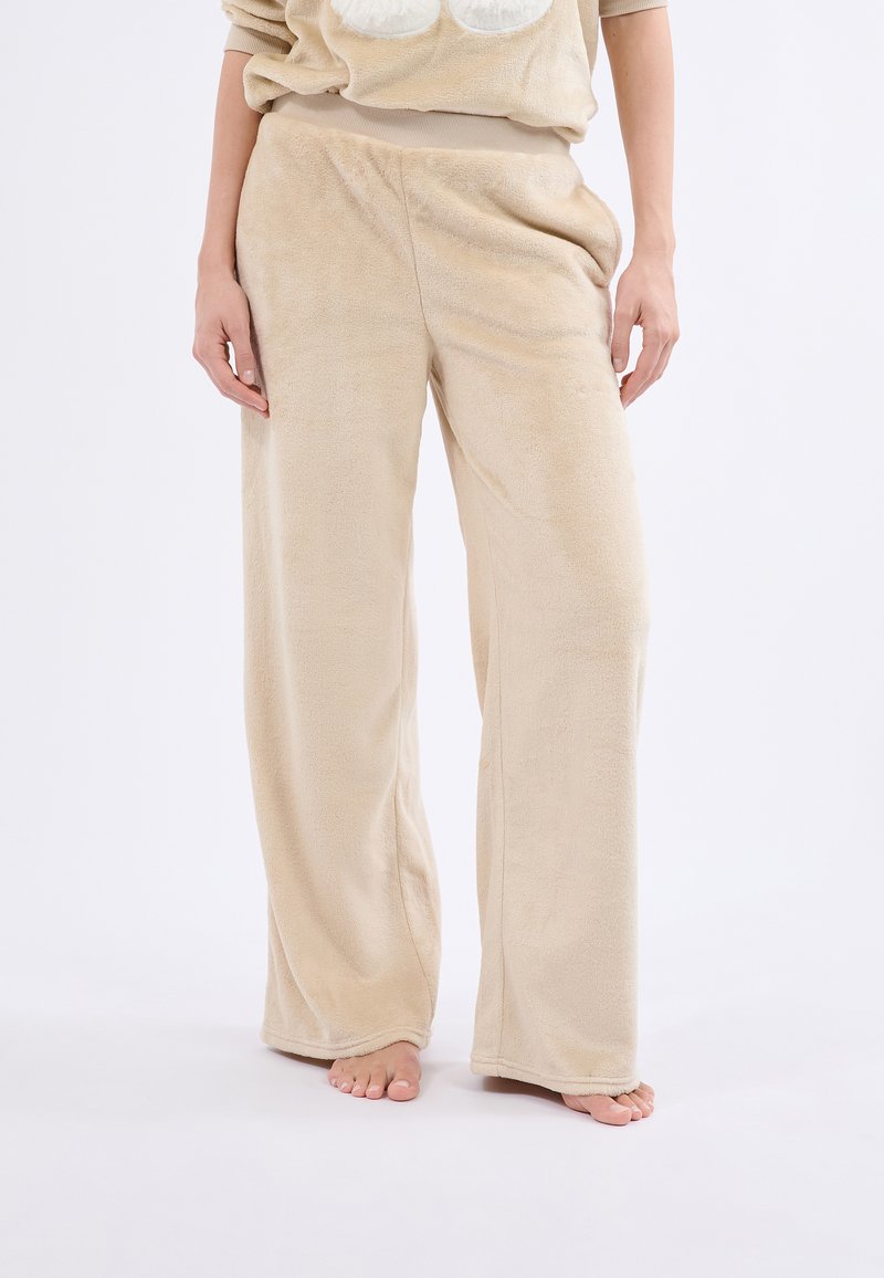 Pantalons de détente en polaire beige avec une coupe évasée, une texture douce et une taille élastique, sans motifs ni éléments métalliques visibles.