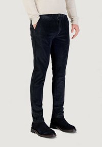 Pantaloni in velluto a coste blu navy dal taglio aderente, caratterizzati da righe verticali, tasche laterali e chiusura con bottone e cerniera, abbinati a stivaletti neri alla caviglia.