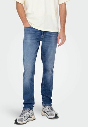 Sininen farkkutakki slim fit -mallilla, jossa on haalistunut pesu, viisi taskua ja ommeltuja yksityiskohtia. Yhdistetty harmaisiin urheilukenkiin.