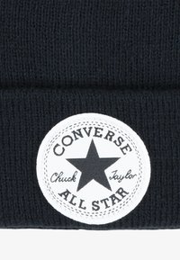 Fekete kötött sapka, fehér, kör alakú folttal, fekete csillaggal és "Converse All Star" felirattal, bordázott textúrával kiemelve.