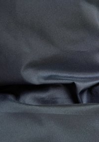 Czarna tkanina o gładkiej, błyszczącej fakturze, z subtelnymi fałdami i różnymi odcieniami ciemnej szarości, wskazującymi na głębię i miękkość.