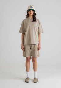 Beige, oversized pamut póló és hozzáillő sort, textúrált felülettel. Krémszínű sapkával párosítva, zöld napernyővel és logó részlettel.