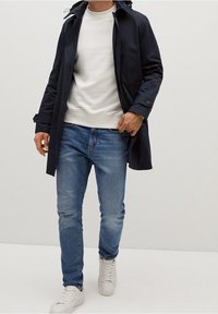 Laivastonsininen trenssitakki, beige collegepaita, vaaleansiniset farkut ja valkoiset tennarit. Sileää kangasta, rento istuvuus ja casual-tyyli.