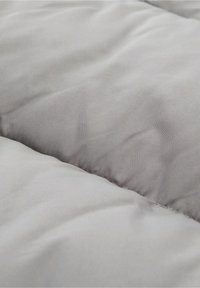 Szary pikowany materiał o gładkiej fakturze, z przeszyciami tworzącymi miękki, wyściełany wygląd.