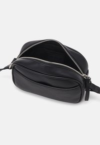Czarna skórzana torba na ramię o zaokrąglonym kształcie, z srebrnym zamkiem błyskawicznym i przednią kieszenią. Wnętrze podszyte i z logo marki.