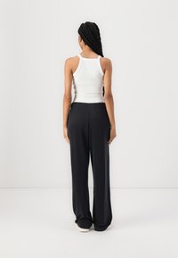 Valge top, millel on reguleeritavad rihmad, koos lõtvade tumehallide pükstega. Rõivastusel on mugav elastne vöökoht.