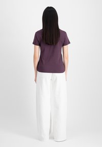 T-shirt violet à manches courtes et ajusté, associé à un pantalon large blanc. Le tissu semble doux, sans motifs ni accents visibles.