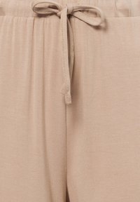 Licht beige joggers met een zachte, gladde textuur, een elastische tailleband met een striksluiting, en gestikt detail langs de tailleband.