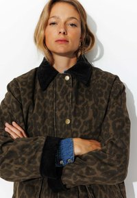 Veste à imprimé léopard dans des tons terreux, col en velours côtelé, boutons dorés, poignets en denim bleu, coupe décontractée avec un design oversize.