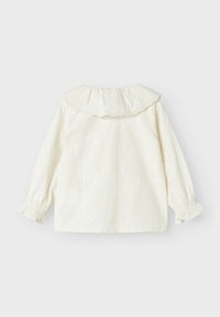 Blusa bianca a maniche lunghe con colletto scallop, motivo floreale testurizzato e polsini arricciati. Tessuto morbido con una finitura liscia.