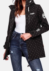 Svart vattentät jacka med huva, med ett subtilt handmönster, blixtlåsfickor och justerbara dragskor i nederkant. Kombineras med jeans.