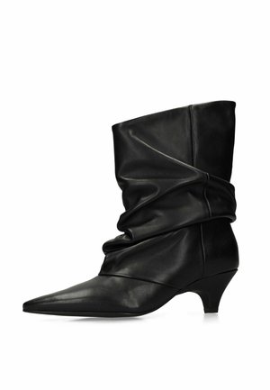 Schwarzer Lederstiefel bis zur Mitte der Wade mit spitzer Spitze, lockerem Schaft und kleinem Kätzchenabsatz.