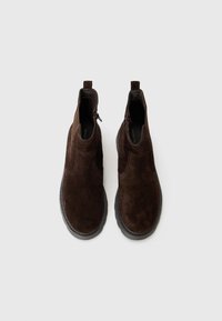 Bottines en suede marron avec une surface texturée, des panneaux élastiques sur les côtés et une fermeture éclair sur le côté. Semelle épaisse en caoutchouc noir pour l'adhérence.