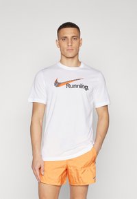 Camiseta blanca de manga corta con el logo de Nike en naranja y texto "Running"; combinada con pantalones cortos texturizados de un naranja brillante.