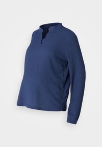 Blå, langermet topp med henley-hals, laget av teksturert stoff. Har en løs passform og spaltinger i sidene for komfort og bevegelighet.