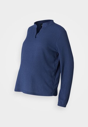 Camisola azul de manga longa com decote henley, feita de um tecido texturizado. Apresenta um corte solto e fendas laterais para conforto e facilidade de movimento.