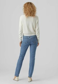 Witte gebreide trui, blauwe spijkerbroek en beige schoenen met blokhak. De spijkerbroek heeft achterzakken en een rechte pijp. Trui van gestructureerde stof.