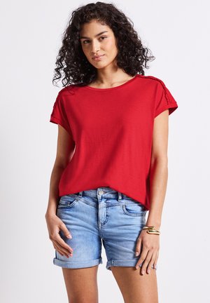 Haut rouge à manches courtes avec des accents texturés aux épaules, coupe décontractée et col rond, associé à des shorts en denim bleu clair.
