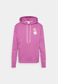 Fialová mikina s kapsou ve stylu klokana, bílými šňůrkami na stažení a grafikou sedmikrásky s logem Nike na hrudi. Měkká textilní struktura.