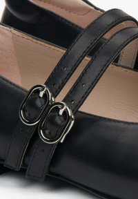 Zwarte leren schoenen met twee smalle banden met zilveren gespen. Het interieur is van zacht beige, wat het ontwerp van de schoen benadrukt.