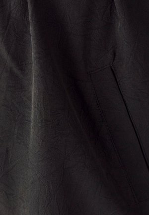 Tessuto nero con una superficie testurizzata, dotato di una tasca laterale e lievi pieghe. Il materiale appare leggero e morbido.