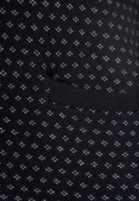 Svart stickad tyg med ett upprepande diamantmönster i grått och vitt. Inkluderar ett texturerat ribbat band för stretch.