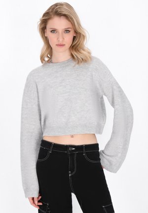 Lichtgrijze cropped sweater met een ronde halslijn en lange mouwen, gemaakt van een zachte stof. Gecombineerd met high-waisted zwarte jeans met witte stiksels.
