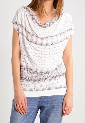 Top blanco con escote drapeado, que presenta un diseño de patrón geométrico en azul y marrón en el pecho y el dobladillo. Tejido suave, mangas cortas.