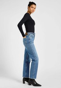 Lichtblauwe rechtlopende jeans van denim met een bruinleren label op de tailleband, gecombineerd met een zwarte strakke lange mouwtop en zwarte laarzen.