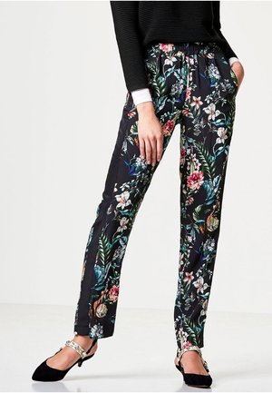 Vrouw draagend zwarte bloemenbroek, zwart langermig shirt en zwarte lage hakken met enkelsluiting.