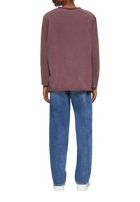 Oversized Langarm-T-Shirt in muted Pflaume, aus weichem Stoff, kombiniert mit blauen Jeans, die einen entspannten Schnitt und gerade Beine haben.