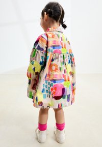 Vestito colorato realizzato in tessuto con motivi astratti. Presenta maniche ampie, un colletto e una gonna a balze. Indossato con calzini rosa e scarpe bianche.