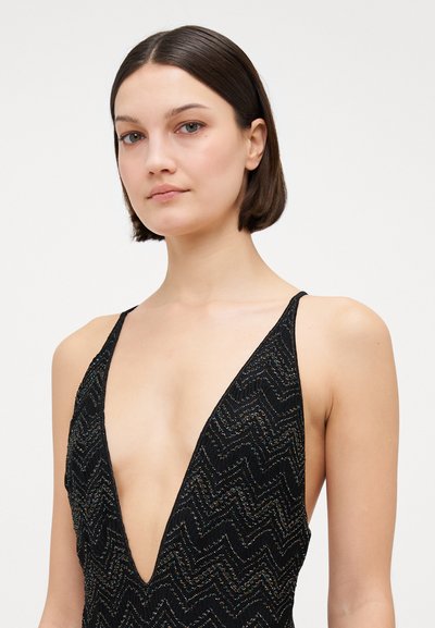 Melnas kleitas ar dziļu V-veida kaklu, aprīkota ar teksturētu zigzaga rakstu un smalkām metalizētām detaļām, regulējamām plānām siksnām.