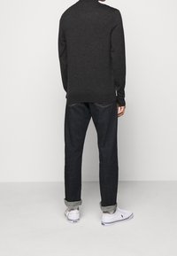 Grå stickad tröja med ribbat fåll, i kombination med mörkblå denimjeans. Vita sneakers med blå accent, uppvikt vid anklarna.