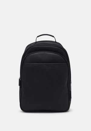 Sac à dos noir avec une poignée de transport sur le dessus, un compartiment principal zippé et une grande poche avant sur fond clair.
