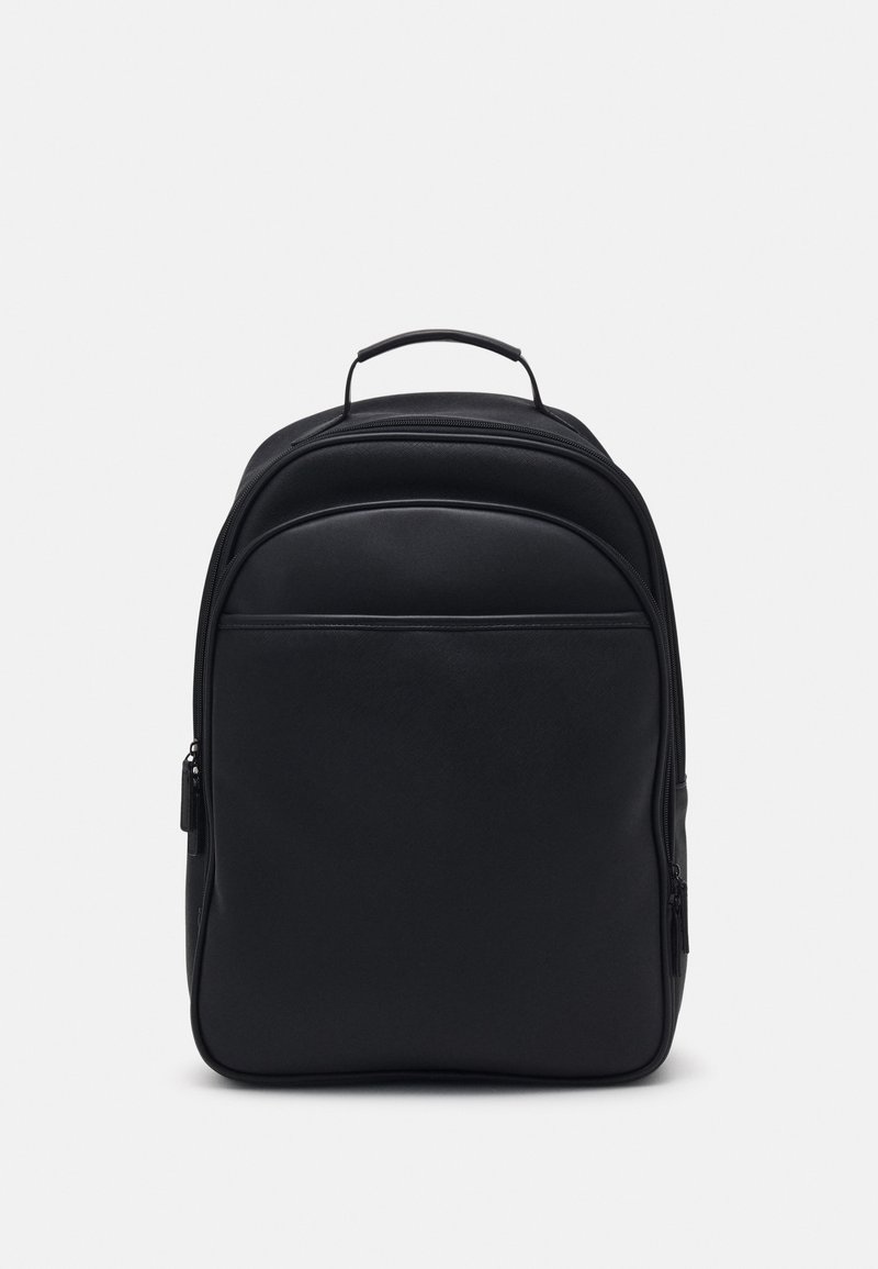 Sac à dos noir avec une poignée de transport sur le dessus, un compartiment principal zippé et une grande poche avant sur fond clair.