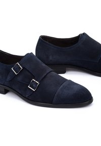 Zapatos de ante azul marino con un acabado suave, presentan acentos de doble hebilla plateada y un diseño de puntera en cap en un tacón bajo negro.