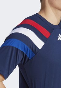 Marineblauw sportshirt met rood, wit en blauw gestreepte accenten op de schouders. Gladde stof met een ronde hals en het Adidas-logo.